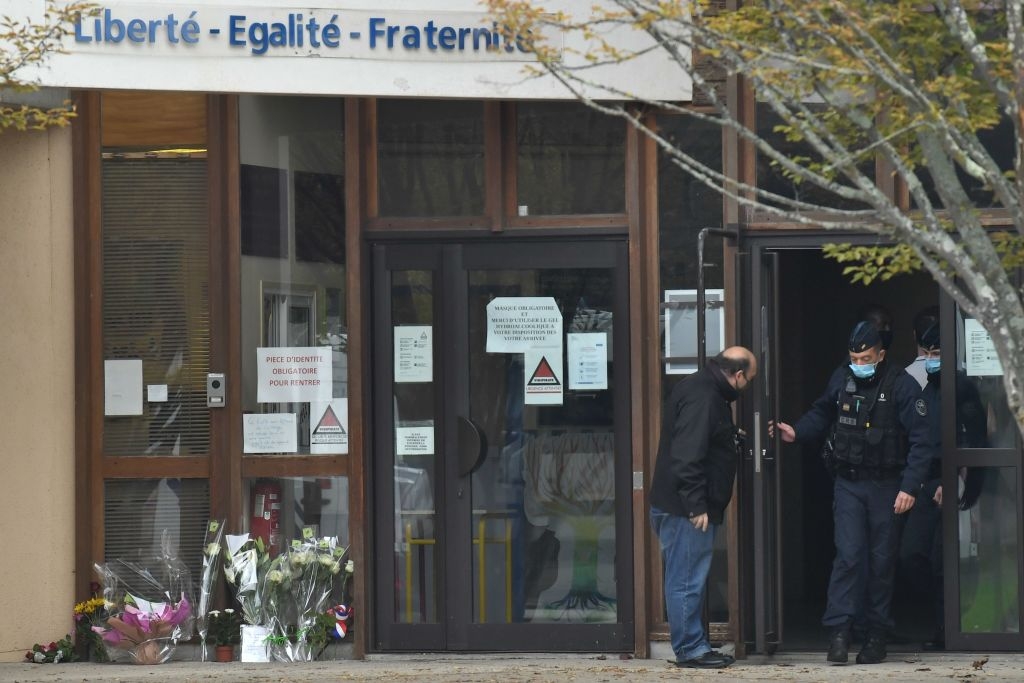 TOPSHOT - French CRS police (Compagnies Republicaines de Securite) walk out of a middle school in Conflans-Sainte-Honorine, 30kms northwest of Paris, on October 17, 2020, next to flowers displayed after a teacher was decapitated by an attacker who has been shot dead by policemen. - The man suspected of beheading on October 16 ,2020 a French teacher who had shown his students cartoons of the prophet Mohammed was an 18-year-old born in Moscow and originating from Russia's southern region of Chechnya, a judicial source said on October 17. Five more people have been detained over the murder on October 16 ,2020 outside Paris, including the parents of a child at the school where the teacher was working, bringing to nine the total number currently under arrest, said the source, who asked not to be named. The attack happened at around 5 pm (1500 GMT) near a school in Conflans Saint-Honorine, a western suburb of the French capital. The man who was decapitated was a history teacher who had recently shown caricatures of the Prophet Mohammed in class. (Photo by Bertrand GUAY / AFP) (Photo by BERTRAND GUAY/AFP via Getty Images)