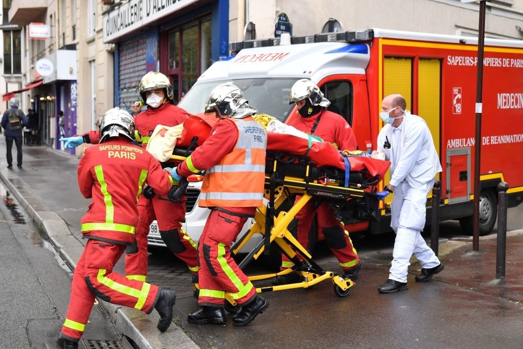 TOPSHOT - French firefighters carrying an injured person near the former offices of the French satirical magazine Charlie Hebdo following an alleged attack by a man wielding a machete in Paris on September 25, 2020. - The threats coincide with the trial of 14 suspected accomplices of the perpetrators of the massacres at Charlie Hebdo and a Jewish supermarket that left a total of 17 dead. (Photo by Alain JOCARD / AFP) (Photo by ALAIN JOCARD/AFP via Getty Images)